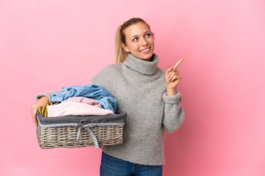 Pembe arka planda izole edilmiş çamaşır sepetini tutan genç bir kadın harika bir fikre işaret ediyor.