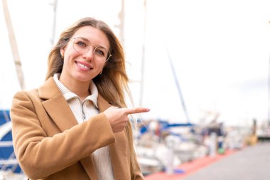 Genç, güzel, sarışın kadın açık havada, gözlüklü ve işaret eden.
