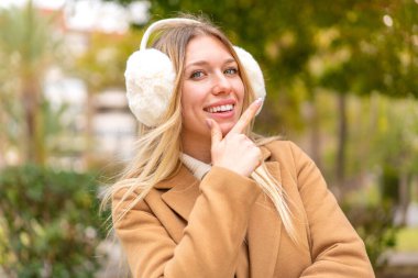 Sarışın, güzel bir kadın. Açık havada kışın kuklalar takıyor. Gülümsüyor.