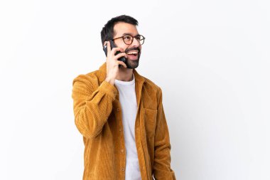 Beyaz arka planda kadife ceket giyen beyaz saçlı, sakallı yakışıklı bir adam cep telefonuyla sohbet ediyor.