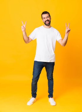 Sarı arka planda sakallı bir adamın uzun pozu zafer işaretini iki eliyle gösteriyor.