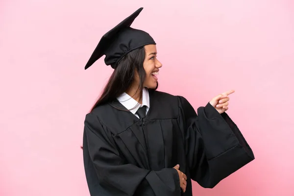 Young university Colombian woman graduate isolated on pink background pointing finger to the side and presenting a product