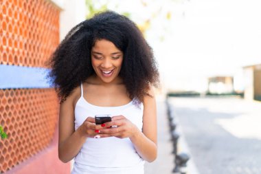 Dışarıdaki genç Afrikalı Amerikalı kadın cep telefonuyla mesaj yolluyor.