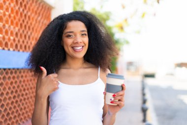 Afro-Amerikalı genç bir kadın açık havada kahvesini yudumluyor çünkü iyi bir şey oldu.