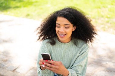 Açık havada cep telefonu kullanan genç Afrikalı Amerikalı kadın.