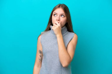 Genç Litvanyalı bir kadın mavi arka planda izole edilmiş. Şüpheleri var ve kafası karışmış bir yüz ifadesi var.