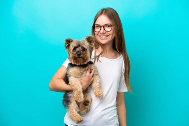 Genç Litvanyalı bir kadın mavi arka planda mutlu bir ifadeyle bir köpeği tutuyor.