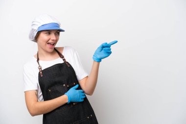 Balıkçı kadın önlük takıyor, parmağıyla kenarı işaret ediyor ve bir ürün sunuyor.