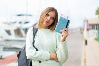 Genç, güzel, sarışın bir kadın elinde pasaport tutarken üzgün bir ifadeyle.