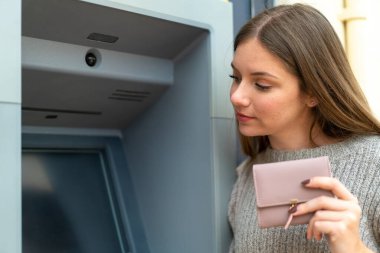 Genç, sarışın bir kadın ATM kullanıyor.