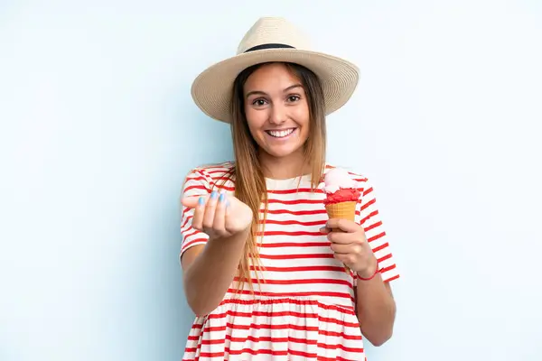 Young caucasian woman holding an ice cream isolated on blue background inviting to come with hand. Happy that you came