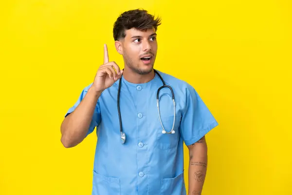 若い外科医の男性は 指を上げながら解決策を実現しようとする黄色の背景に隔離されました — ストック写真