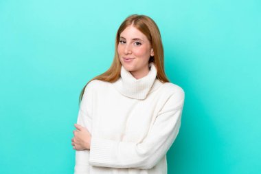 Genç kızıl saçlı kadın mavi arka planda yalnız gülüyor.