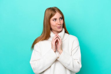 Genç kızıl saçlı kadın mavi arka planda bir şeyler planlıyor.