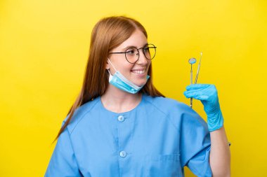 Sarı arka planda izole edilmiş genç kızıl saçlı dişçi kadın.