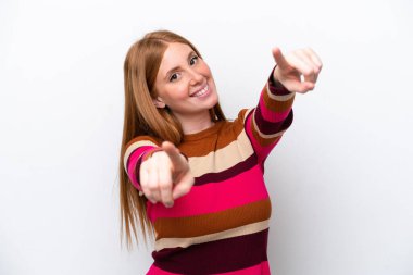 Beyaz arka planda izole edilmiş genç kızıl saçlı kadın mutlu bir ifadeyle ön tarafı işaret ediyor.