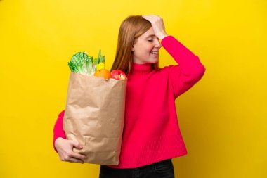 Sarı arka planda izole edilmiş alışveriş torbası tutan genç kızıl saçlı kadın bir şey fark etti ve çözüme niyetlendi.