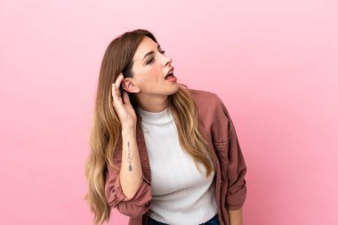 Pembe arka planda izole edilmiş beyaz bir kadın. Kulağına elini sürerek bir şeyler dinliyor.