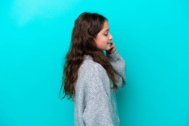 Mavi arka planda izole edilmiş küçük bir kız cep telefonuyla sohbet ediyor.