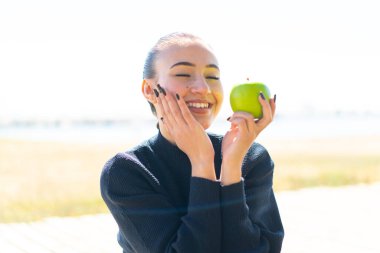 Genç Faslı kız açık havada elinde mutlu bir ifadeyle bir elma tutuyor.
