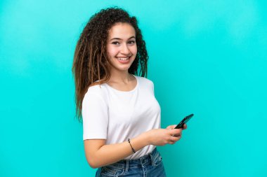Genç Arap kadın mavi arka planda izole edilmiş cep telefonuyla mesaj ya da e-posta gönderiyor