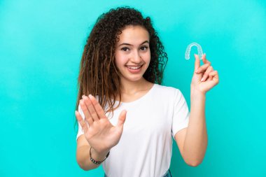 Mavi arka planda izole edilmiş görünmez diş telleri tutan genç Arap kadın mutlu bir ifadeyle selamlıyor.