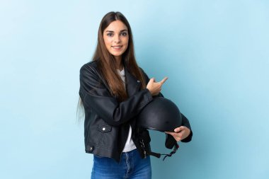 Mavi arka planda izole edilmiş motosiklet kaskı tutan beyaz bir kadın.