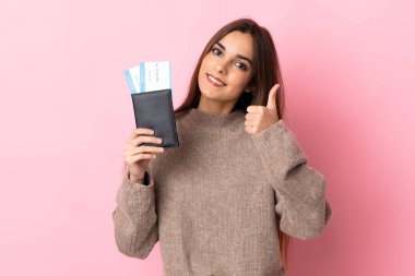 Pembe arka planda izole edilmiş genç beyaz bir kadın. Elinde pasaport ve uçak tutuyor.