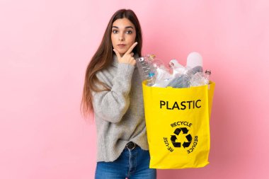 Kafkasyalı genç bir kadın pembe arka planda izole edilmiş plastik şişelerle dolu bir çanta tutuyor.