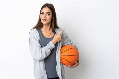 Basketbol oynayan genç bir kadın beyaz arka planda izole edilmiş bir şekilde bir ürünü sunmak için kenarı işaret ediyor.