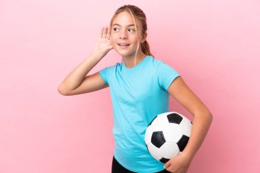 Pembe arka planda izole edilmiş küçük bir futbolcu kız. Kulağına elini sürerek bir şeyler dinliyor.