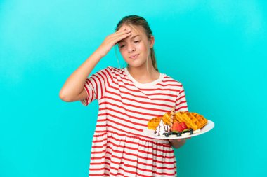 Mavi arka planda baş ağrısıyla izole edilmiş waffle tutan küçük beyaz kız.