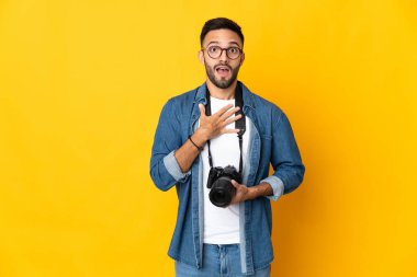 Sarı arka planda izole edilmiş genç fotoğrafçı kız sağa bakarken şaşırmış ve şok olmuştu.