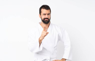 İzole edilmiş beyaz arka planda karate yapan genç adam hayal kırıklığına uğramış ve ön tarafı işaret ediyor.