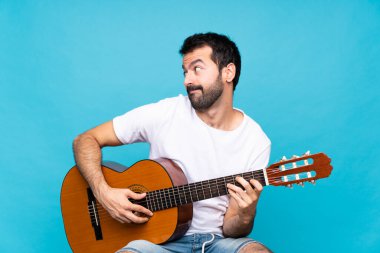 Mavi arka planda gitar çalan genç adam şüpheli hareketler yapıyor.