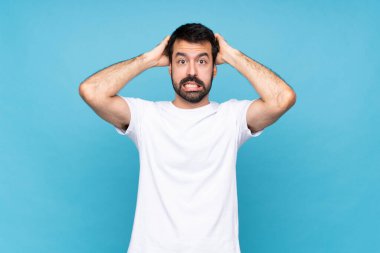 Sakallı genç adam mavi arka planda hayal kırıklığına uğradı ve ellerini başının üstüne koydu.