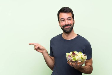 Yeşil duvarın üstünde salatalı yakışıklı genç adam, parmağını yana doğru uzattı.