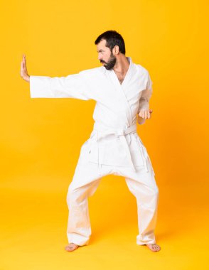 İzole edilmiş sarı arka planda karate yapan bir adamın tam boy fotoğrafı.