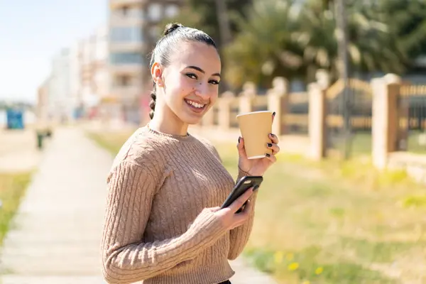 Young moroccan girl  at outdoors using mobile phone and holding a coffee with happy expression