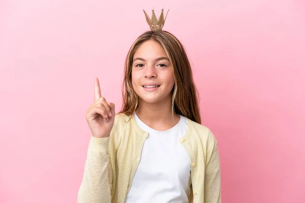 Little princess with crown isolated on pink background showing and lifting a finger in sign of the best