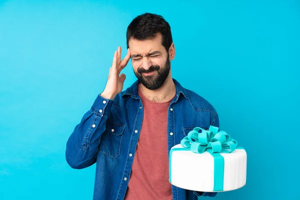 Young handsome man with a big cake over isolated blue background with headache
