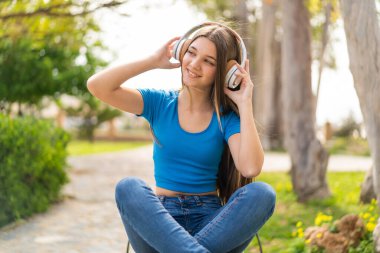 Genç kız açık havada müzik dinliyor.