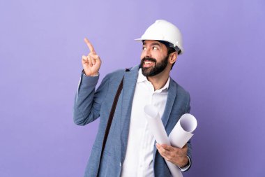 Miğferli genç bir mimar, izole edilmiş mor arkaplanın planlarını tutuyor ve işaret parmağıyla işaret ediyor. Harika bir fikir.