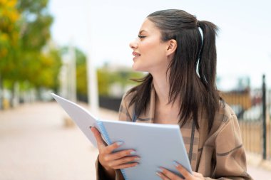 Dışarıda elinde bir defter tutan genç ve güzel bir kadın.