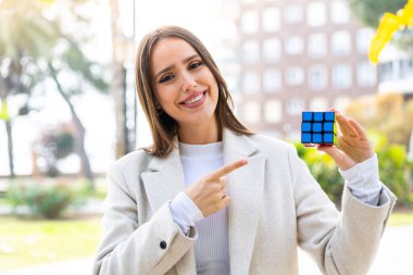 Genç ve güzel bir kadın dışarıda üç boyutlu bir bulmaca küpünü tutuyor ve ona doğrultuyor.