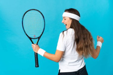 Genç İspanyol kadın, izole edilmiş mavi arka planda tenis oynuyor ve zaferi kutluyor.