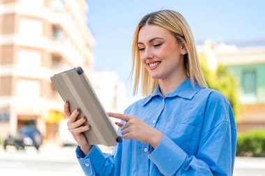 Dışarıdaki güzel sarışın kadın tablet ekranına mutlu bir ifadeyle dokunuyor.