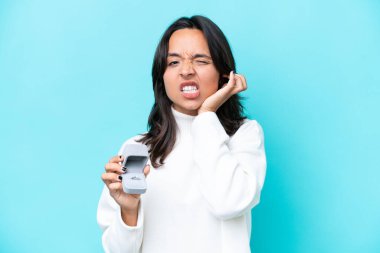 Mavi arka planda izole edilmiş nişan yüzüğünü tutan genç İspanyol kadın hayal kırıklığına uğramış ve kulaklarını kapatmış.