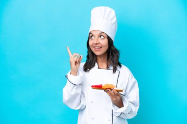 Mavi arka planda saşimi tutan genç İspanyol aşçı kadın harika bir fikre işaret ediyor.