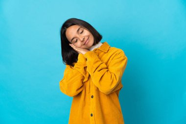 Mavi arka planda izole edilmiş genç Latin bir kadın uyku jesti yapıyor.